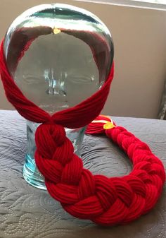 a red rope wrapped around a ball of yarn on a glass vase with a window in the background