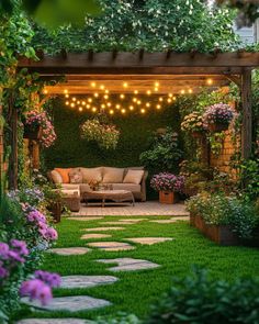 an outdoor living area with lots of greenery and lights strung over the seating area