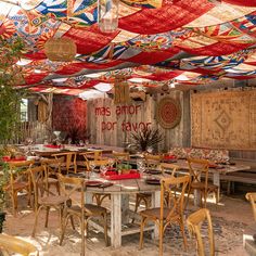 an outdoor dining area with tables, chairs and rugs hanging from the rafters