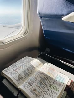 an open book sitting on top of a table next to a window in an airplane