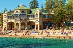 many people are on the beach in front of a large building with green roof and white trim