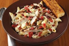 a brown plate topped with pasta and meat next to a piece of bread on top of a wooden table