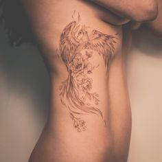 a woman's stomach with a bird and flowers tattoo on her side ribcage