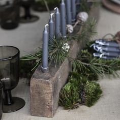 some candles are sitting on top of a piece of wood and surrounded by pine needles