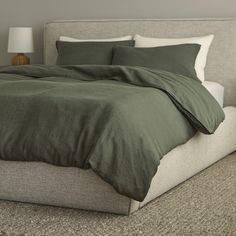 a bed with green sheets and pillows on top of it in a gray room next to a lamp