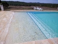 an empty swimming pool with lounge chairs in the background and water running down the side