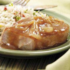 a green plate topped with rice and meat covered in gravy next to a fork