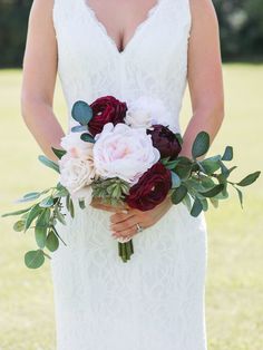 a woman in a wedding dress holding a bridal bouquet with red and white flowers