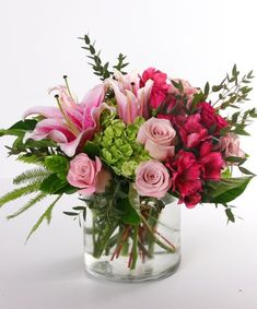 a vase filled with pink and red flowers on top of a white table next to greenery