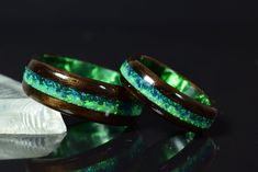 two wooden rings with green and blue glitter inlays sitting on top of each other