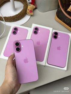 two pink iphones are being held up by someone's hand on a table