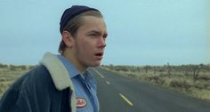 a man standing on the side of a road with a blue jacket over his shoulders