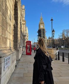 a woman is walking down the sidewalk in front of a red phone booth and big ben