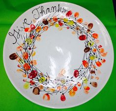 a white plate with an orange and yellow wreath on it that says, give thanks