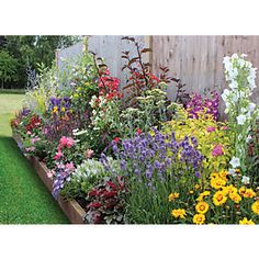 a garden filled with lots of colorful flowers next to a wooden fence and green grass