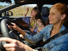 two women are sitting in the driver's seat of a car and one is waving