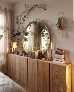 a mirror and some plants on a wooden cabinet in a room with white walls,