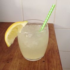 a glass filled with lemonade sitting on top of a wooden table next to a green and white straw