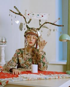 a woman sitting at a table with a deer headpiece on top of her head