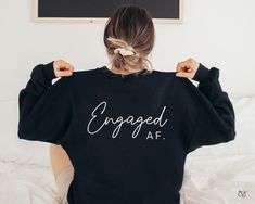 a woman wearing an engaged af sweatshirt on top of a bed with her hands behind her back