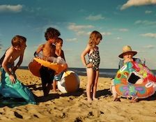 four children playing on the beach with boogie boards