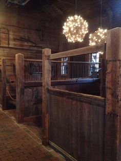 the inside of a barn with lights hanging from it's ceiling and wooden stalls