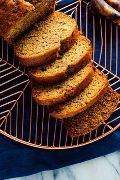 sliced banana bread sitting on top of a wire rack next to bananas and other fruit