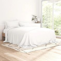 a white bed sitting next to a window on top of a hard wood floored floor