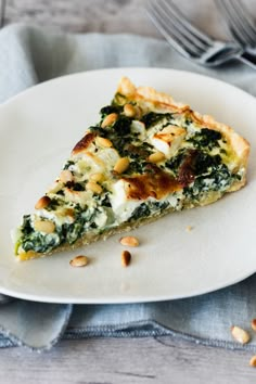 a slice of quiche with spinach and pine nuts on a plate next to a fork