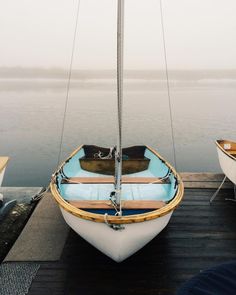 a small sailboat sitting on top of a wooden dock next to the ocean with fog in the sky