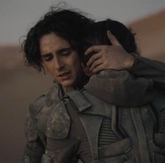 a man is hugging another man in the desert