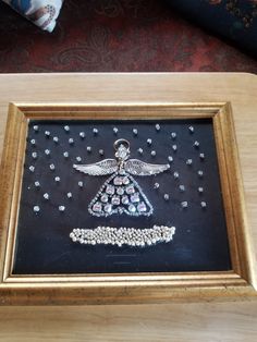 an embroidered angel ornament is displayed in a gold frame on a wooden table