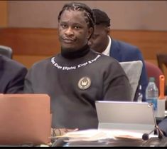 a man sitting at a table with a laptop in front of him and other people behind him