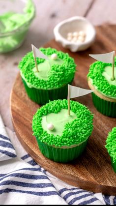 cupcakes with green frosting and white flags on them sitting on a wooden platter