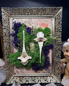 an ornate frame is adorned with moss and flowers as well as two white spoons