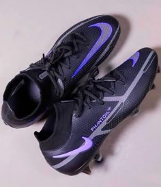 a pair of black and purple soccer shoes on a white surface with one shoe in the air