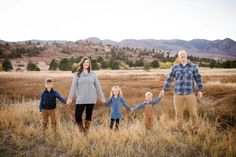 a family holding hands and walking through tall grass with mountains in the background at sunset