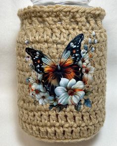 a crocheted jar with a butterfly painted on the side and flowers around it