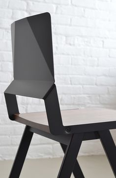 a black chair sitting on top of a wooden table next to a white brick wall