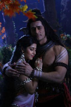 a man and woman dressed in costumes hugging each other while standing next to trees with leaves on them