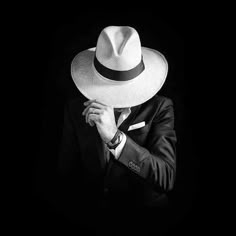 a man in a suit and hat with his hand on his face