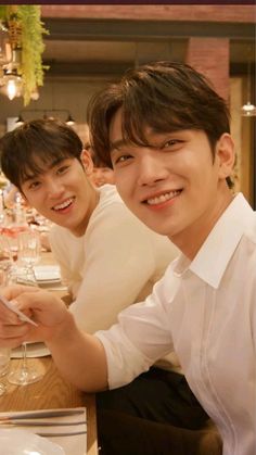 two young men sitting at a table with wine glasses