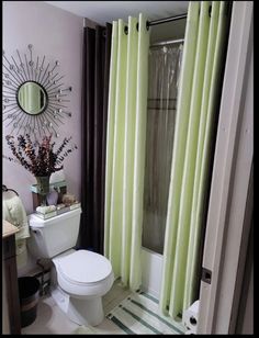 a white toilet sitting in a bathroom next to a green curtained shower stall with a mirror on the wall