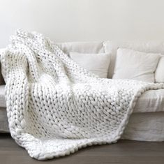 a white blanket sitting on top of a couch next to pillows