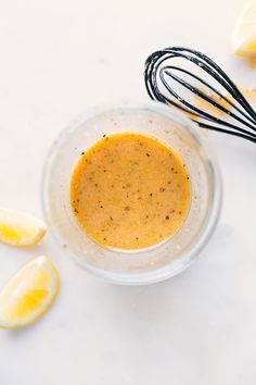 a glass bowl filled with liquid next to lemons and whisks on a white surface