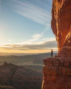 a person standing on the edge of a cliff with mountains in the background at sunset