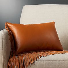 a brown leather pillow sitting on top of a white couch next to a beige chair