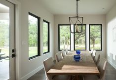 a dining room table with chairs and a vase on it in front of large windows