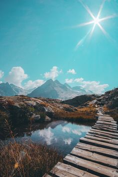 a wooden bridge over a small body of water with mountains in the backgroud