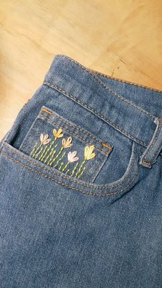 a pair of jeans with embroidered flowers on the back pocket, sitting on a wooden surface